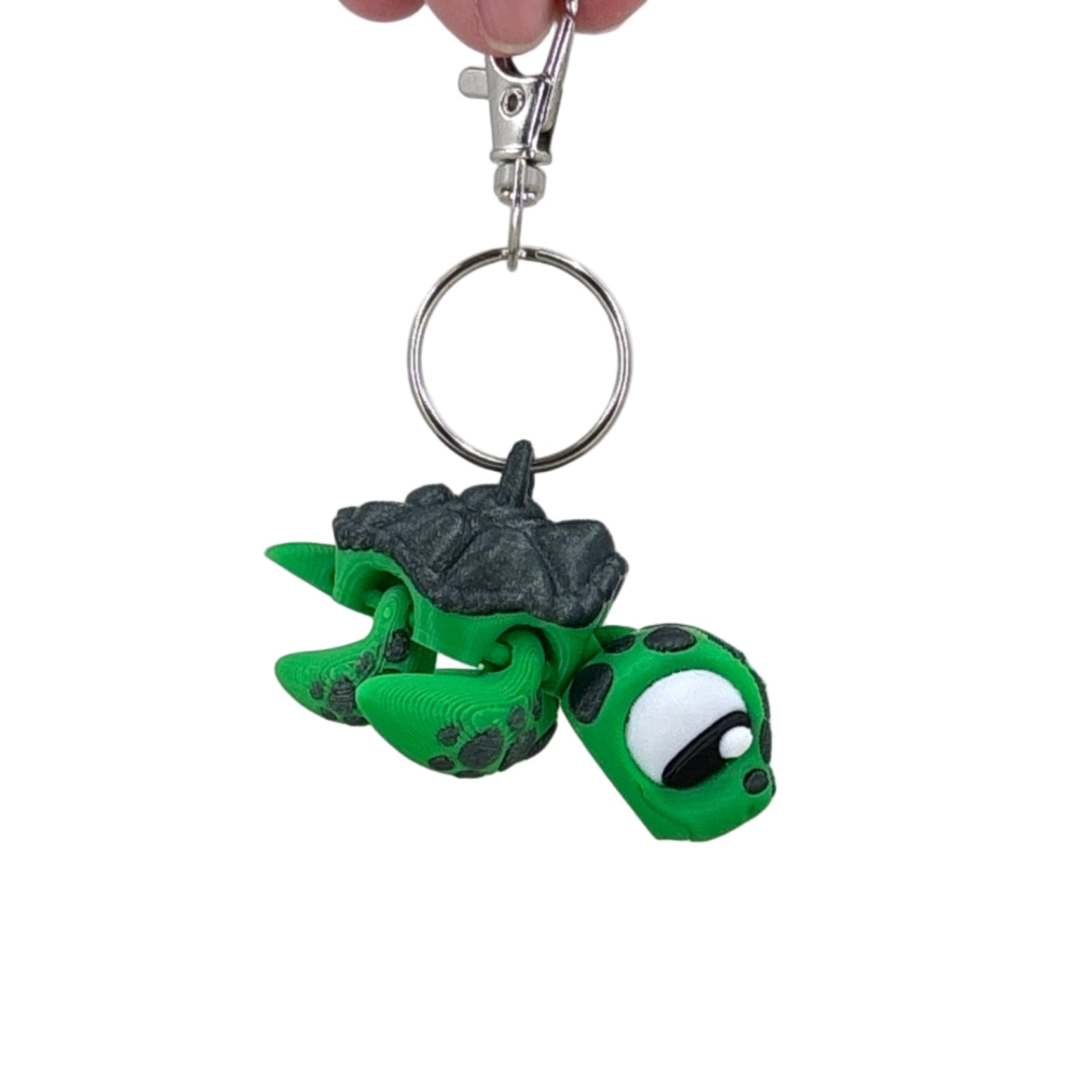 Green turtle keychain held by a hand against a plain background