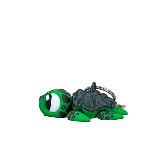 Green turtle keychain with a gray shell on a light beige background