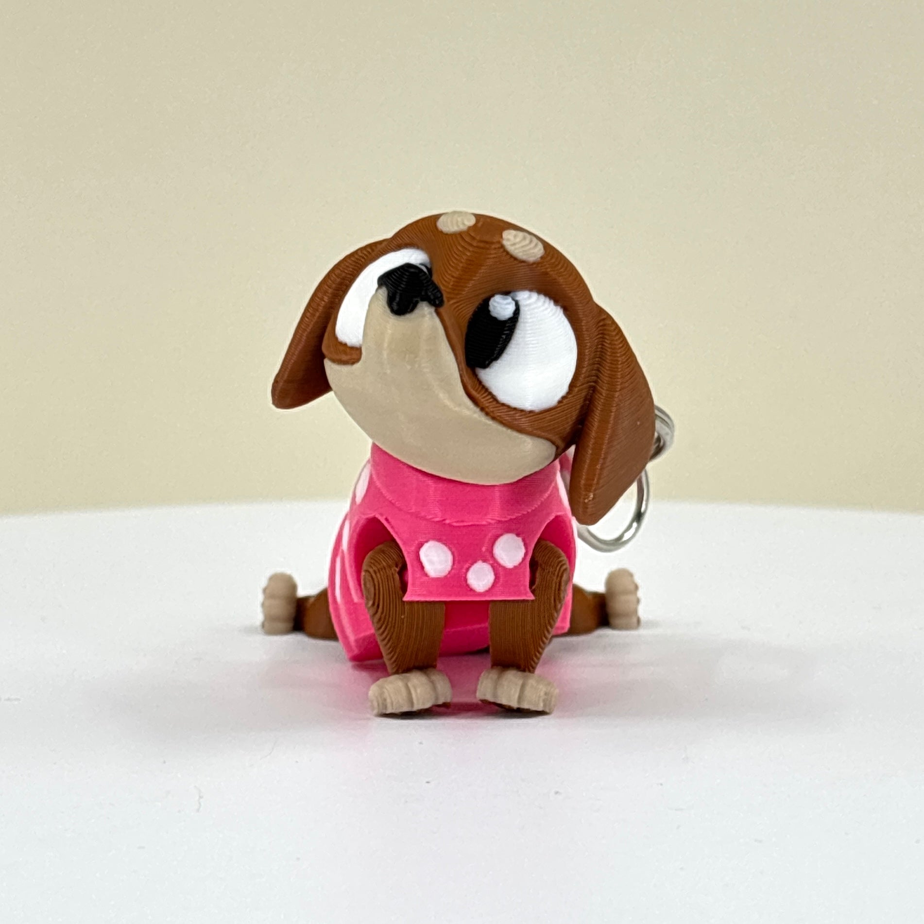 Dog-shaped keychain with a pink outfit on a white surface